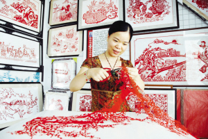 Een vrouw doet aan papierknipkunst: achter haar zijn al voltooide exemplaren te zien.
